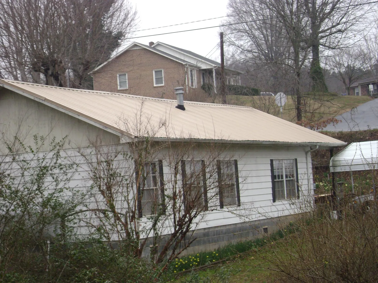 Tan metal roof on a white sided house set into a hillside — Commercial Roofing by Roofing Brothers in Winthrop